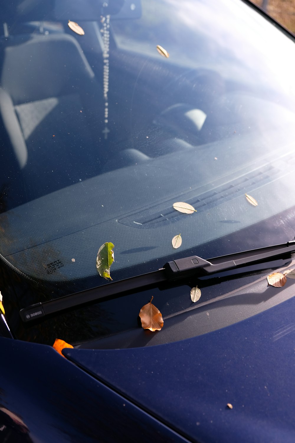 a blue car with leaves on the windshield