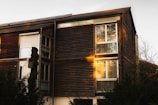 Modern wooden house with large windows reflecting a sunset sky.