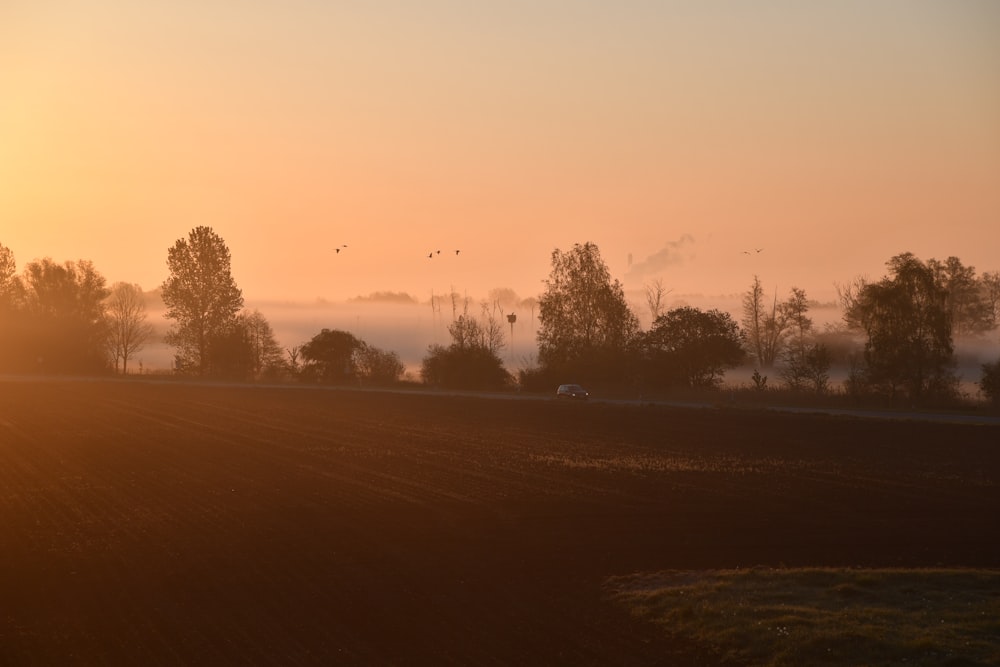 the sun is setting over a farm field