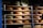 Multiple wheels of cheese are stacked on wooden shelves arranged in rows. The cheeses vary in size and have colorful labels with text and designs. The lighting creates a warm and rustic atmosphere, emphasizing the rich, creamy hues of the cheese.