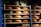 Multiple wheels of cheese are stacked on wooden shelves arranged in rows. The cheeses vary in size and have colorful labels with text and designs. The lighting creates a warm and rustic atmosphere, emphasizing the rich, creamy hues of the cheese.