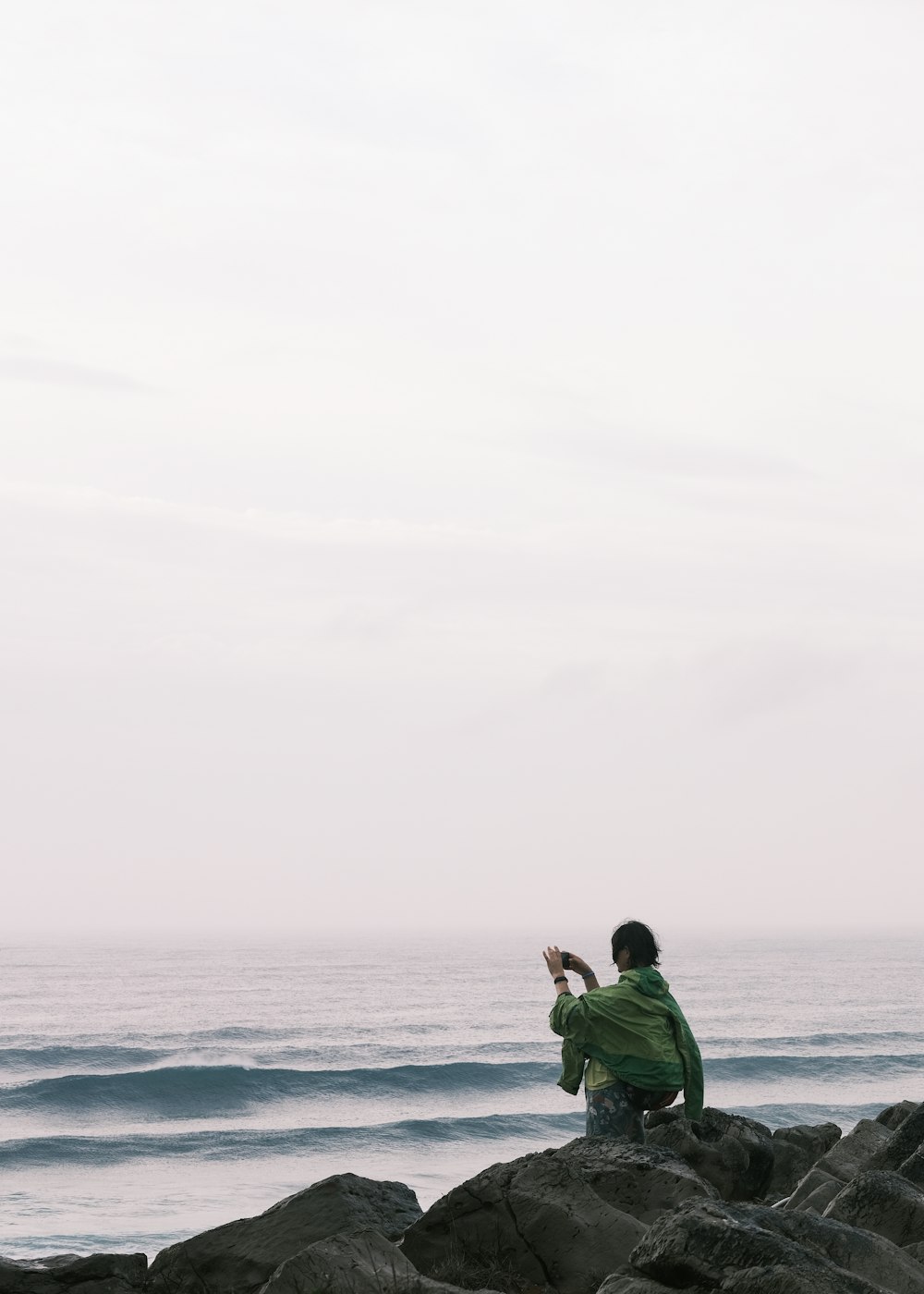 a person sitting on a rock taking a picture of the ocean