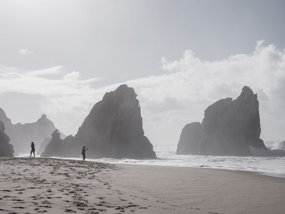 a couple of people standing on top of a sandy beach