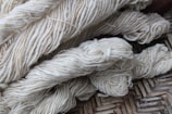 Bundles of cream-colored yarn are laid out, showing various thick strands intertwined and resting on a woven surface.