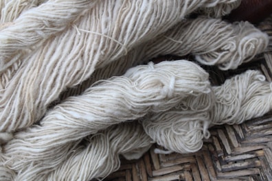 Bundles of cream-colored yarn are laid out, showing various thick strands intertwined and resting on a woven surface.