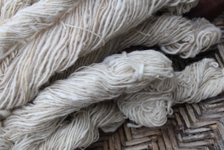 Bundles of cream-colored yarn are laid out, showing various thick strands intertwined and resting on a woven surface.