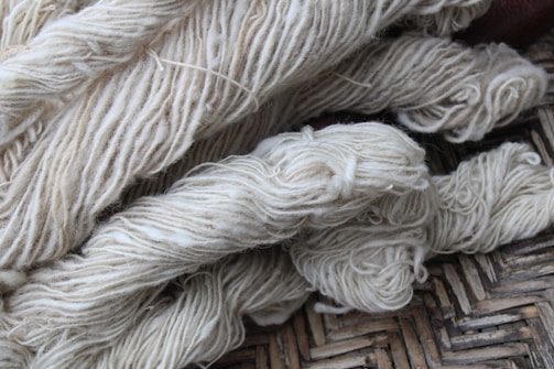 Bundles of cream-colored yarn are laid out, showing various thick strands intertwined and resting on a woven surface.