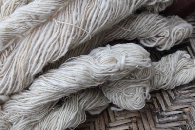 Bundles of cream-colored yarn are laid out, showing various thick strands intertwined and resting on a woven surface.