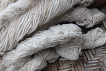 Bundles of cream-colored yarn are laid out, showing various thick strands intertwined and resting on a woven surface.