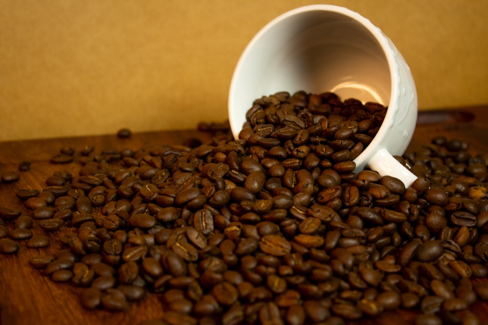 a white cup filled with coffee beans on top of a wooden table