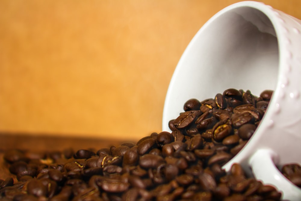 a white cup filled with coffee beans on top of a wooden table