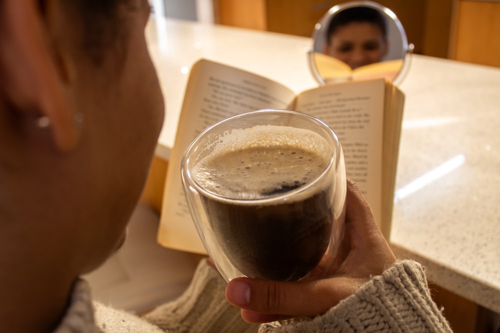 a man holding a glass of coffee in front of an open book