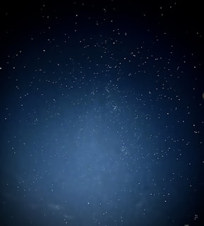A vast night sky dotted with numerous stars. The image captures the beauty of the cosmos, with a deep blue tone and scattered celestial bodies sparkling against the backdrop.