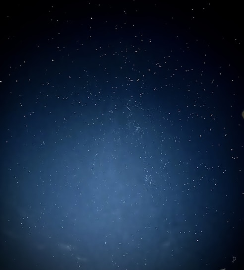 A vast night sky dotted with numerous stars. The image captures the beauty of the cosmos, with a deep blue tone and scattered celestial bodies sparkling against the backdrop.