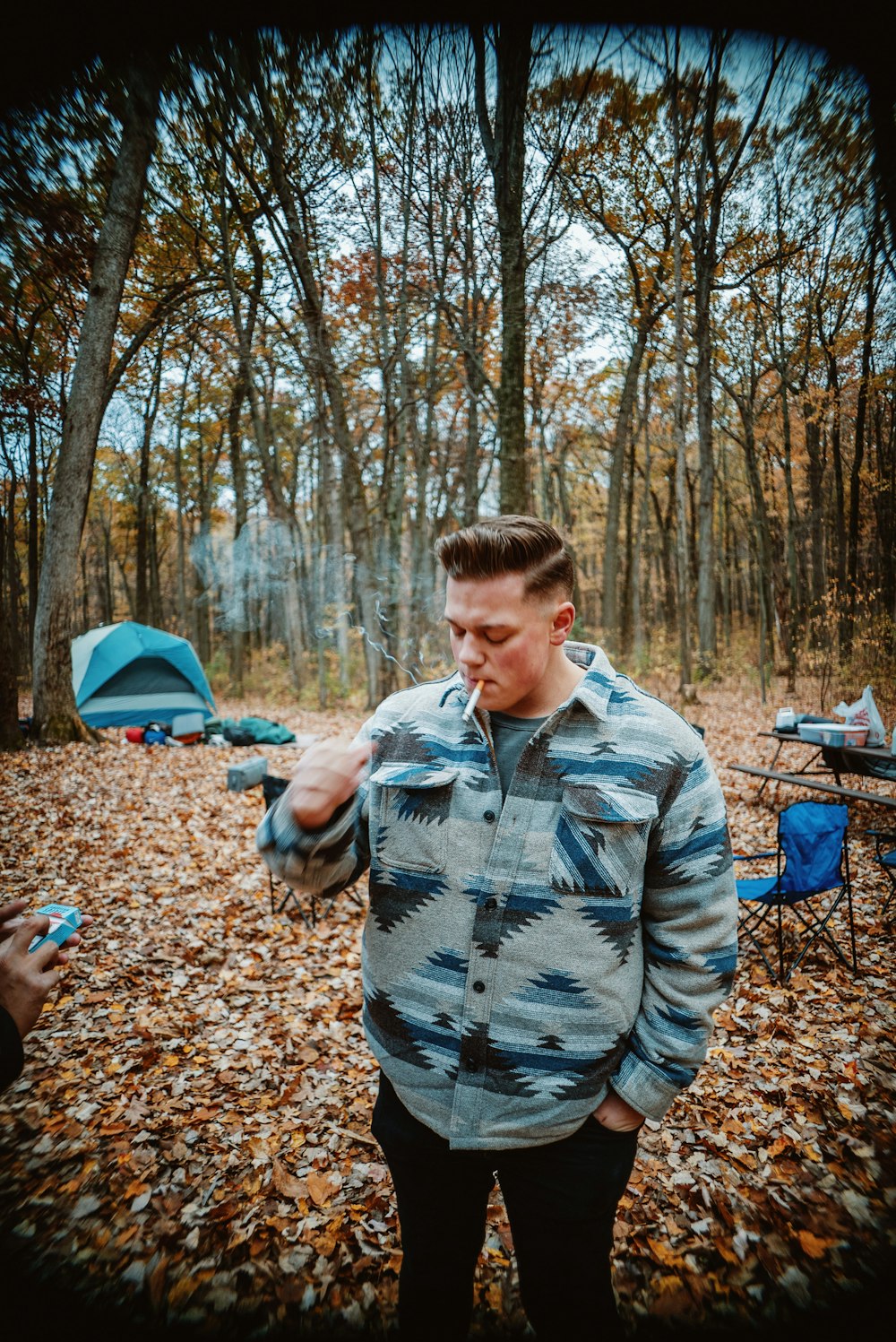 a man standing in the woods with a cigarette in his mouth