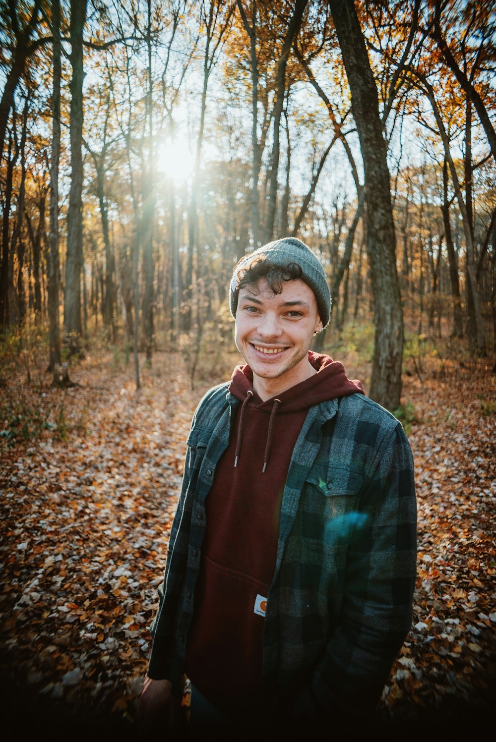 a young man standing in a forest with leaves on the ground