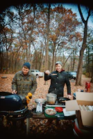 Lore and Jose cooking outside their camper surrounded by lush green forest.