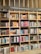A bookshelf filled with a variety of books categorized under Ibero-American literature. The shelves are organized with books displayed upright and stacked, showcasing colorful covers and titles. The structure is wooden with sections divided by horizontal and vertical beams.