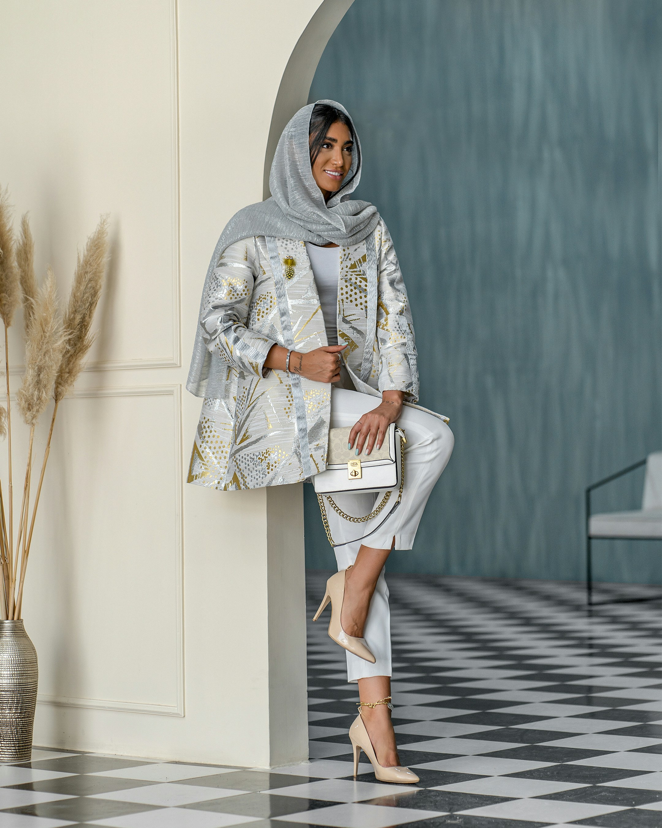 a woman in a white and silver outfit leaning against a wall