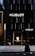 A storefront of a high-end watch brand featuring the name Hublot in bold letters on a sleek, dark facade. Two people are walking on the sidewalk, with one carrying an orange shopping bag and the other a beige handbag. The entrance to the store is illuminated, showcasing a modern and luxurious interior.