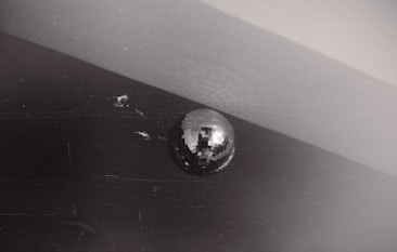A disco ball with reflective facets is suspended from the ceiling, casting faint shadows. The image has a vintage, grainy texture and is in black and white.