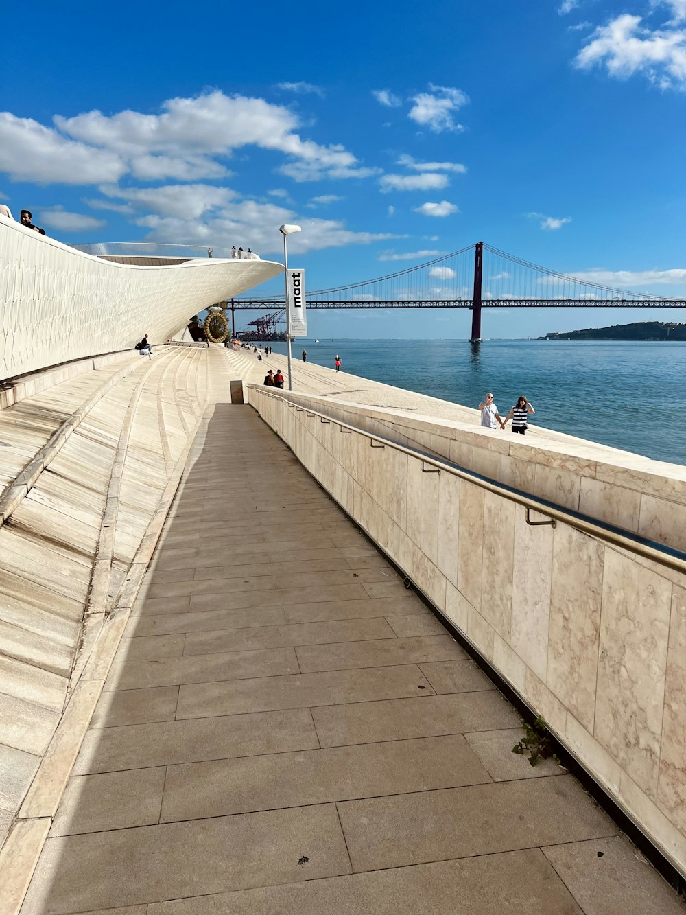 a walkway next to a body of water with a bridge in the background