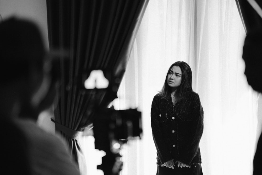 a black and white photo of a woman standing in front of a curtain