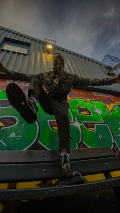 Male model sporting sleek odike streetwear against a city graffiti wall at sunset.