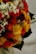 A vibrant floral arrangement featuring a mix of colorful dried flowers, including bright yellow and red blooms, small white and pink blossoms, and some green foliage. The textures vary from soft petals to spiky and fuzzy elements, creating a rich visual tapestry.