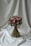 A bouquet of flowers is elegantly arranged with a mix of pink, purple, and green hues. The bouquet is tied with a maroon ribbon and is set against a softly draped white fabric backdrop, creating a serene and sophisticated presentation.