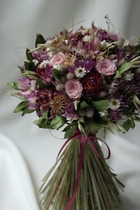 A soft mauve ribbon tied around a finished bouquet with natural greenery.