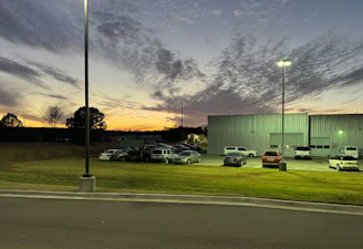 Modern industrial warehouse exterior at sunset with dramatic lighting and trucks parked.