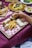 A wooden tray on a red checkered cloth holds rolled flatbreads and crispy french fries. A hand is dipping one of the flatbreads into a small bowl of white sauce. Other dishes in the background include skewered meat with rice on a round wooden platter and small plates of appetizers.