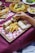 A wooden tray on a red checkered cloth holds rolled flatbreads and crispy french fries. A hand is dipping one of the flatbreads into a small bowl of white sauce. Other dishes in the background include skewered meat with rice on a round wooden platter and small plates of appetizers.