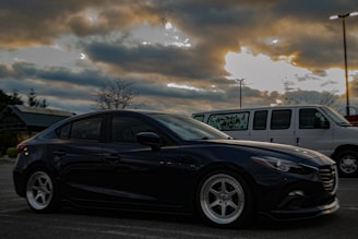 A sleek black crew transport van parked outside a film set under overcast skies.