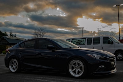 A sleek black crew transport van parked outside a film set under overcast skies.