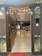 An intricately decorated entryway with a garland of marigold and yellow flowers hanging above a wooden door. The inside view reveals a well-lit interior with glossy marble flooring, modern ceiling designs, and contemporary furniture. Decorative items and soft lighting add to the opulent ambiance.