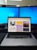 A workspace setup featuring a laptop displaying a webpage with various images, flanked by two large monitors with blue desktop backgrounds.