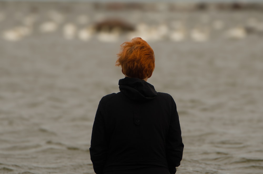 a woman with red hair standing in front of a body of water