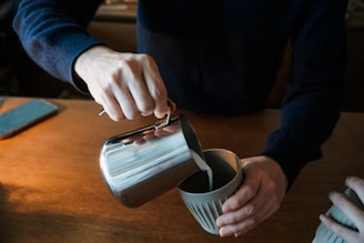 Hands gently pouring fresh milk into a traditional clay pot on a farmhouse table.