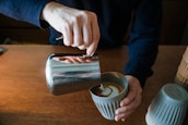 Barista pouring latte art into a ceramic cup on a rustic wooden counter.
