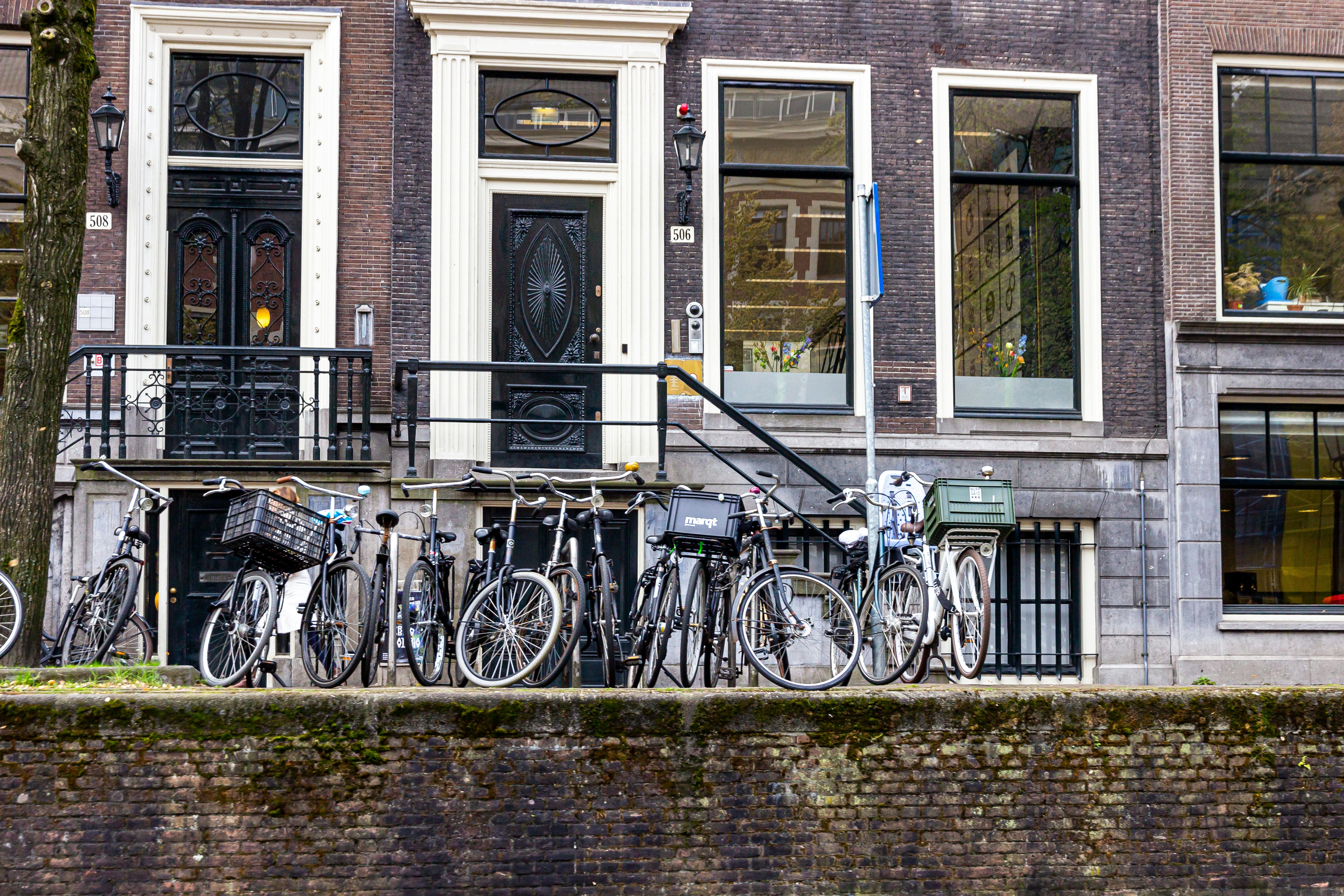 a row of bikes parked next to each other in front of a building, Bicycles and river canals on the streets of Amsterdam