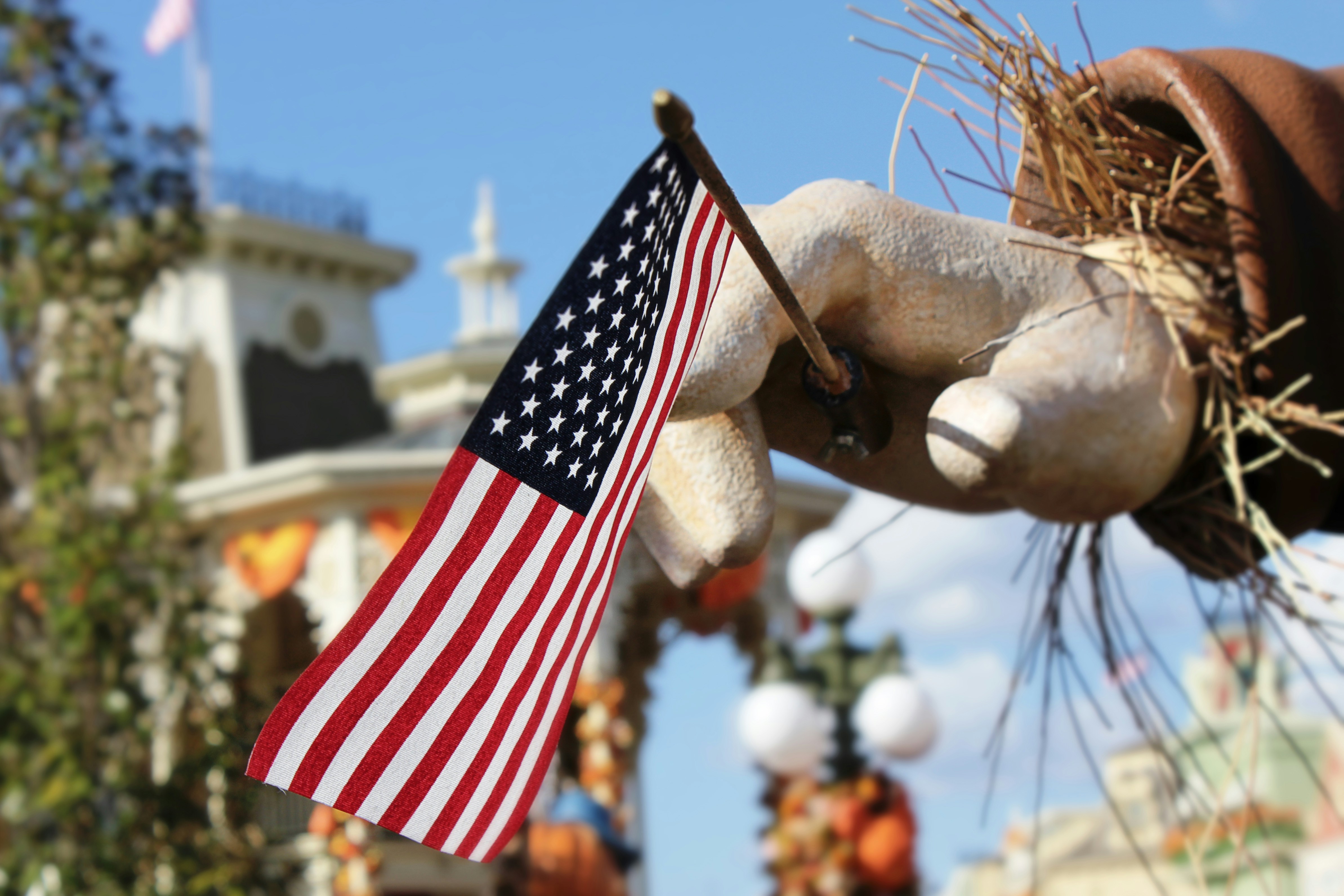 a hand holding an american flag in front of a building, Scarecrow holding an America flag.