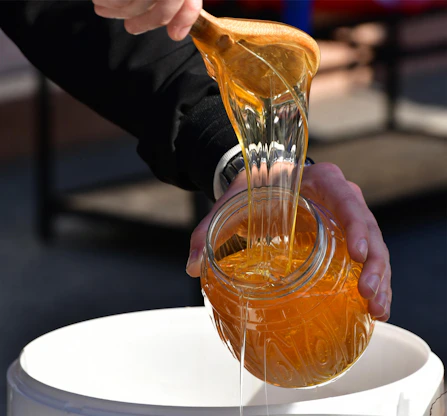 Golden raw honey dripping slowly from a wooden spoon into a glass jar.
