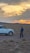 Smiling traveler standing beside a safari jeep in the Namibian desert at sunset.