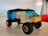 A small toy vehicle made from colorful interlocking plastic bricks sits on a smooth surface. The vehicle has four wheels and a roof made of translucent blue bricks. The body of the vehicle is composed of black, yellow, white, and blue bricks.