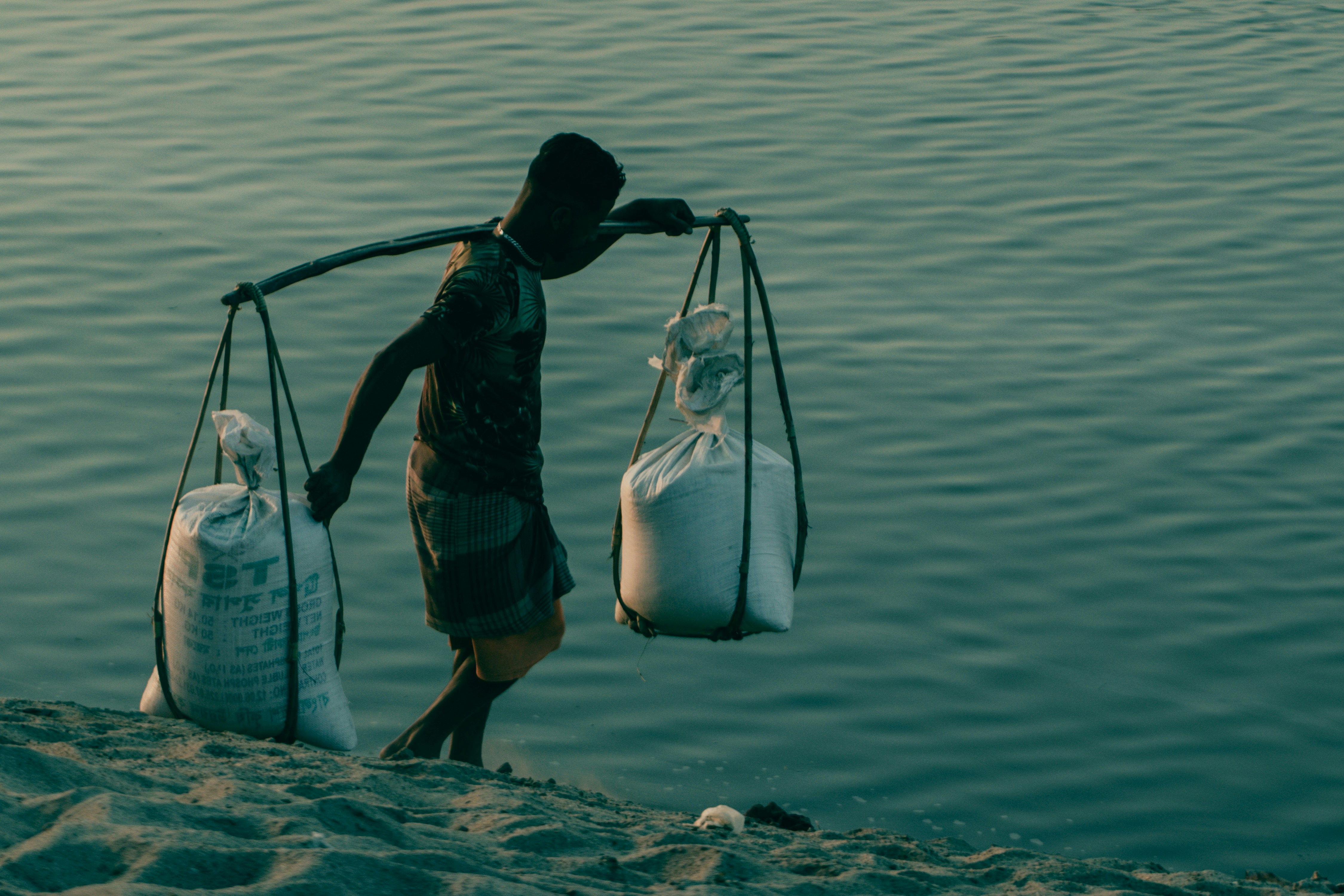 A man carrying two bags of sand on a beach photo Free River Image on