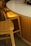 A close-up view of a white table with a smooth, rounded edge accompanied by wooden chairs that have a light golden hue. The table is set against an interior with soft, warm lighting that casts a gentle glow on the furniture.