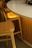 A close-up view of a white table with a smooth, rounded edge accompanied by wooden chairs that have a light golden hue. The table is set against an interior with soft, warm lighting that casts a gentle glow on the furniture.