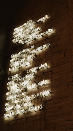 A brick wall with illuminated neon text displaying a message about urban living and nature. The letters are in white, creating a contrast against the dimly lit wall.